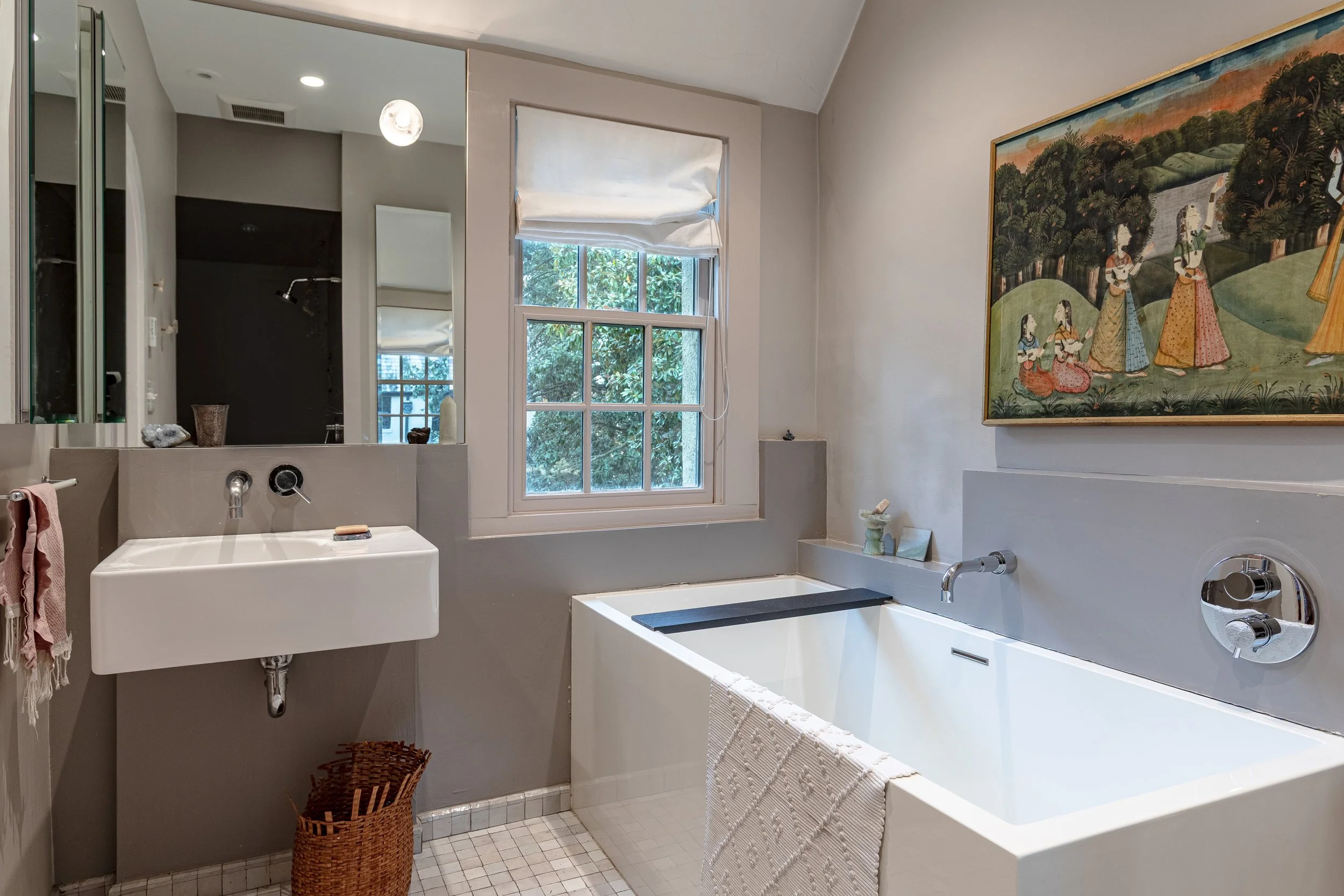 Bathroom with a window, mirror, sink, bathtub, and artwork