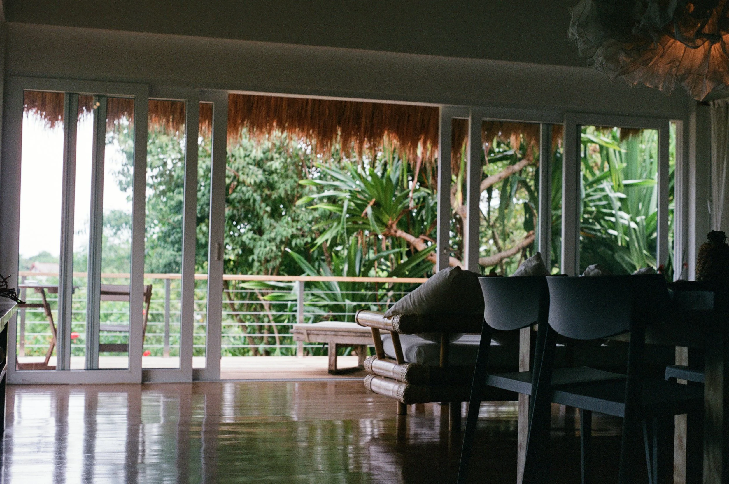 Living room with large sliding glass doors opening to a balcony with greenery outside, furnished with a sofa, chairs, and a coffee table.