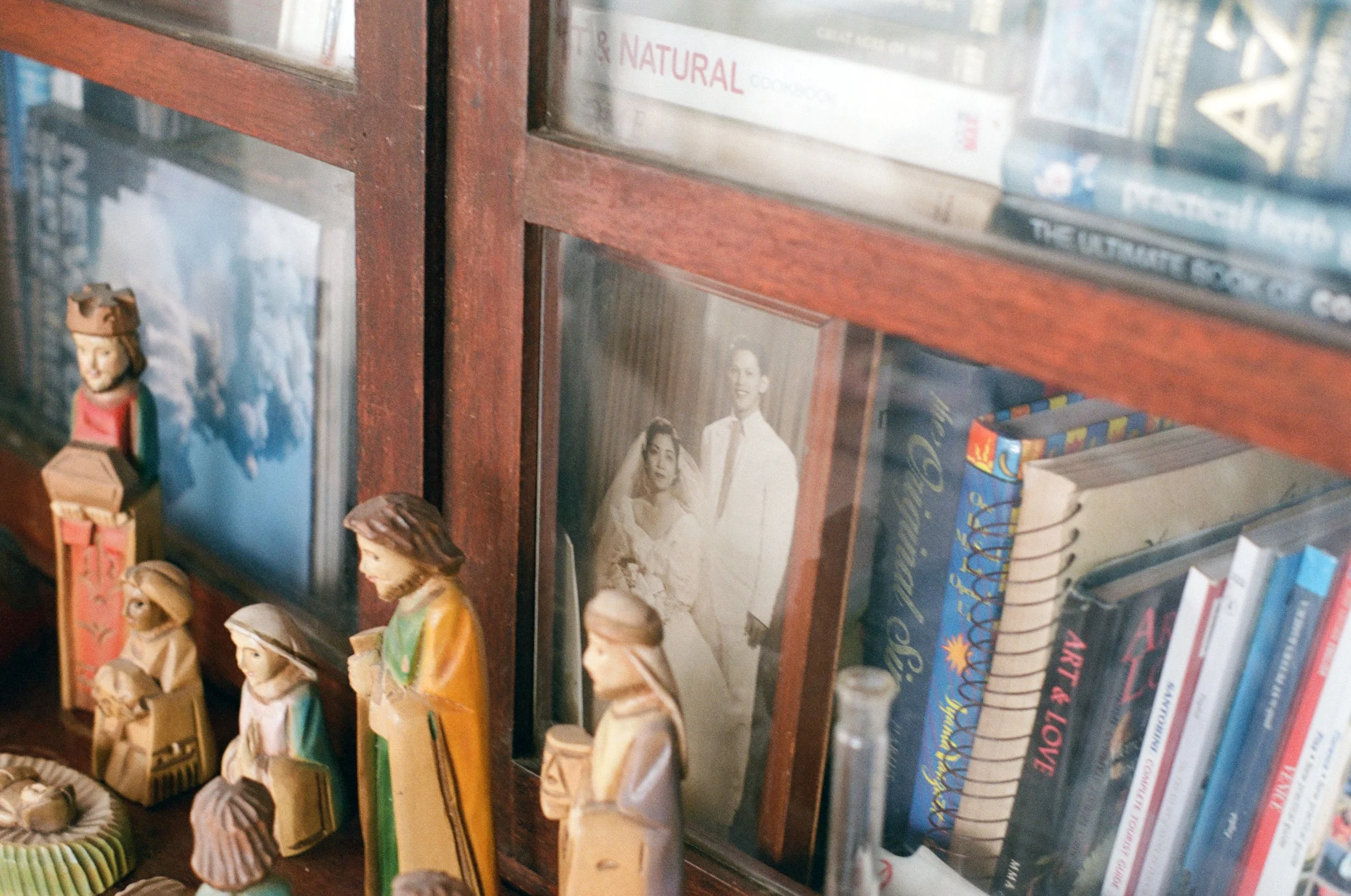 A home bookshelf with a framed black and white photograph of a couple, pewter-colored figures of religious figures, and various books.