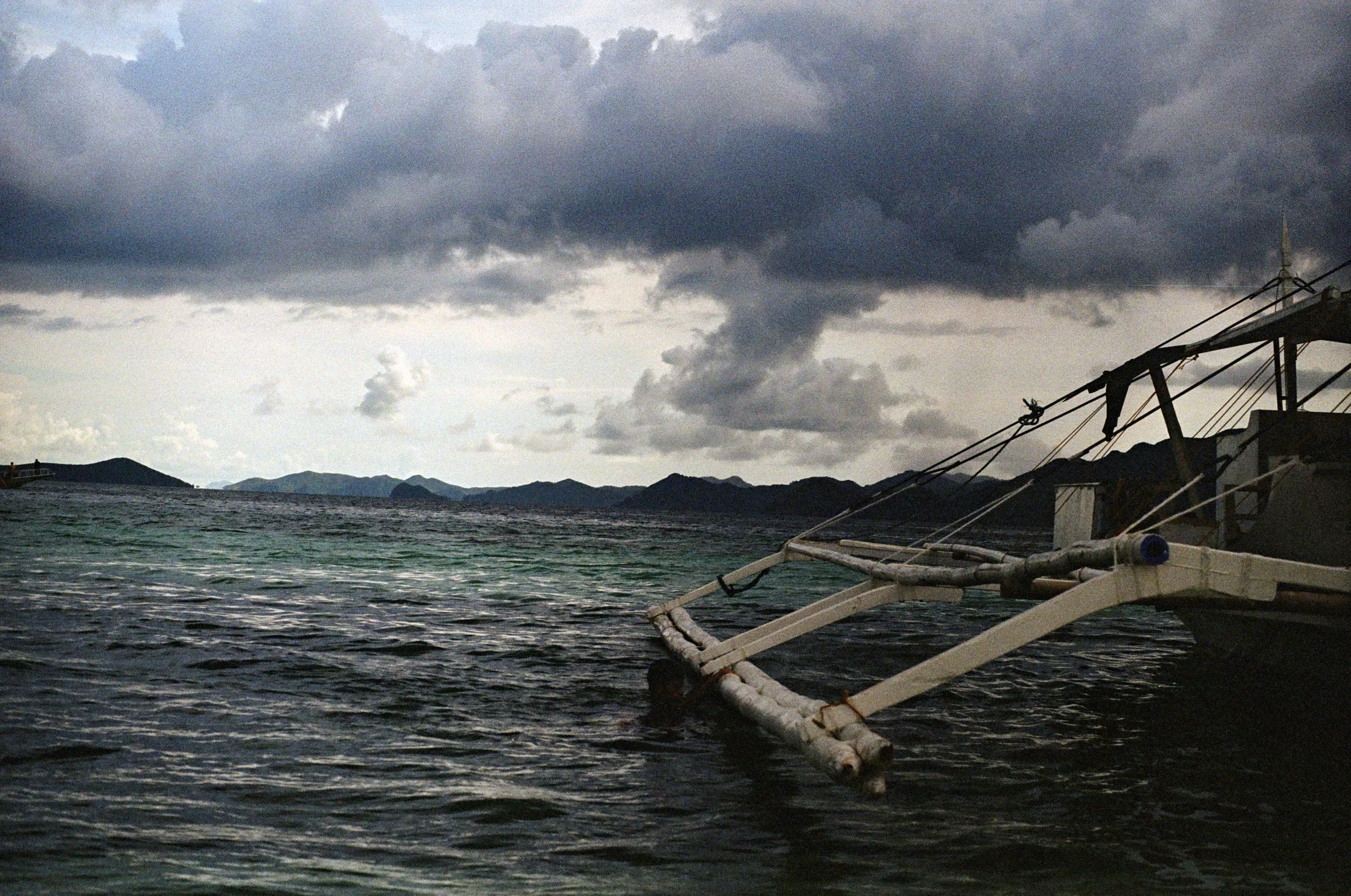 A boat floating in dark water under a cloudy sky, with distant mountains on the horizon.