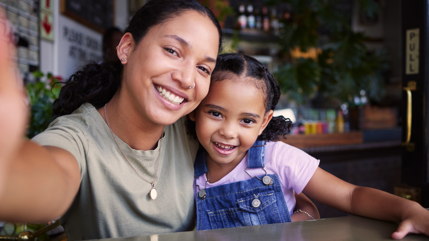Smiling woman and young girl taking a selfie together inside a cafe.