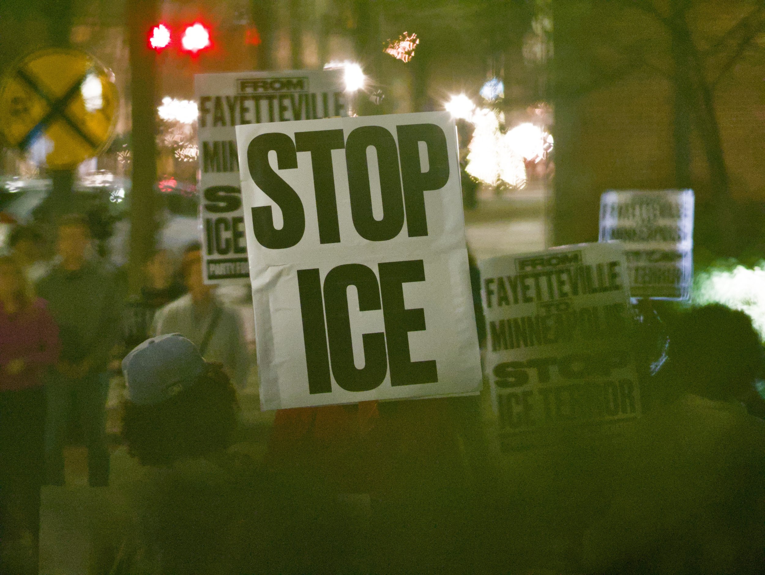 Protesters holding signs that read 'STOP ICE' and 'FROM FAYETTEVILLE MINING'.