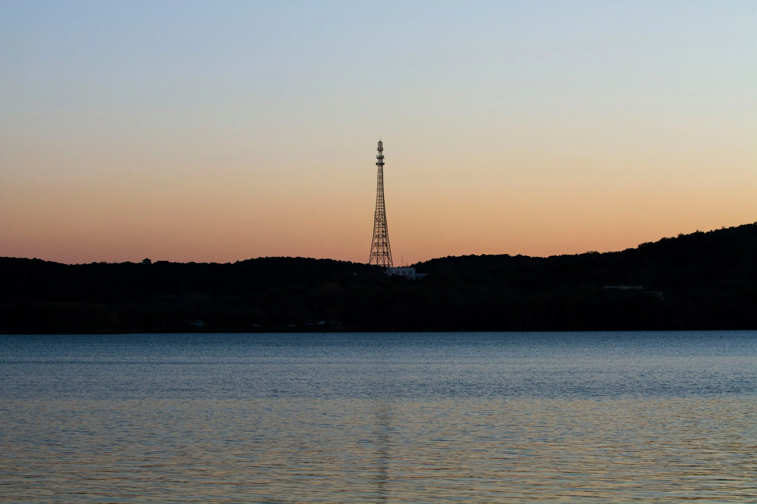 View of a body of water at dusk with a hill in the background and a tall radio tower on top of the hill.