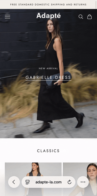 Woman walking outside in a long black dress with a black bag, plants, and a black wall in the background, on a fashion website homepage.