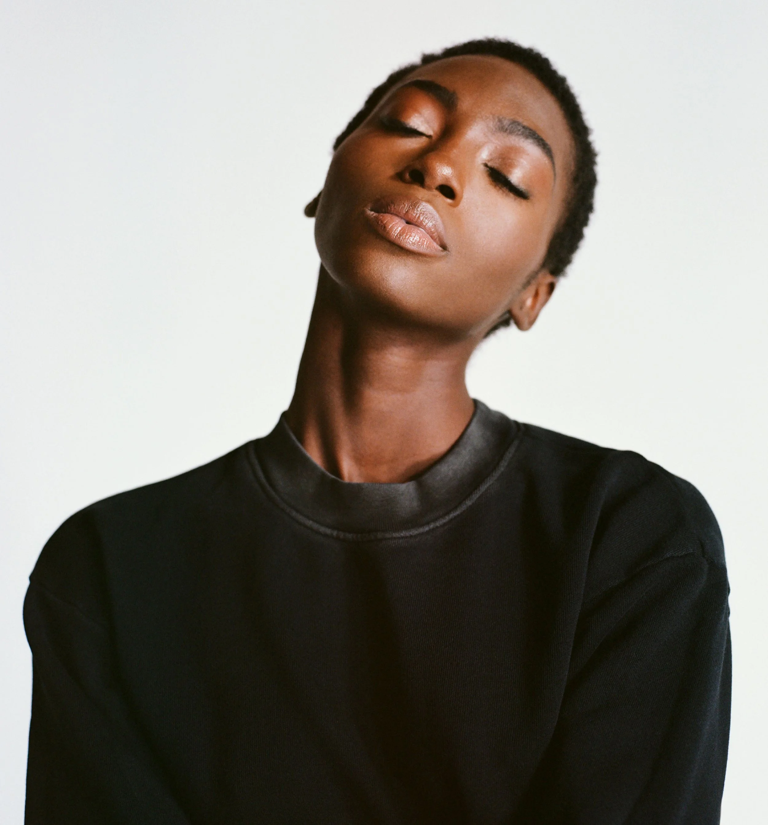 Portrait of a woman with short hair and closed eyes, wearing a black shirt, against a plain white background.