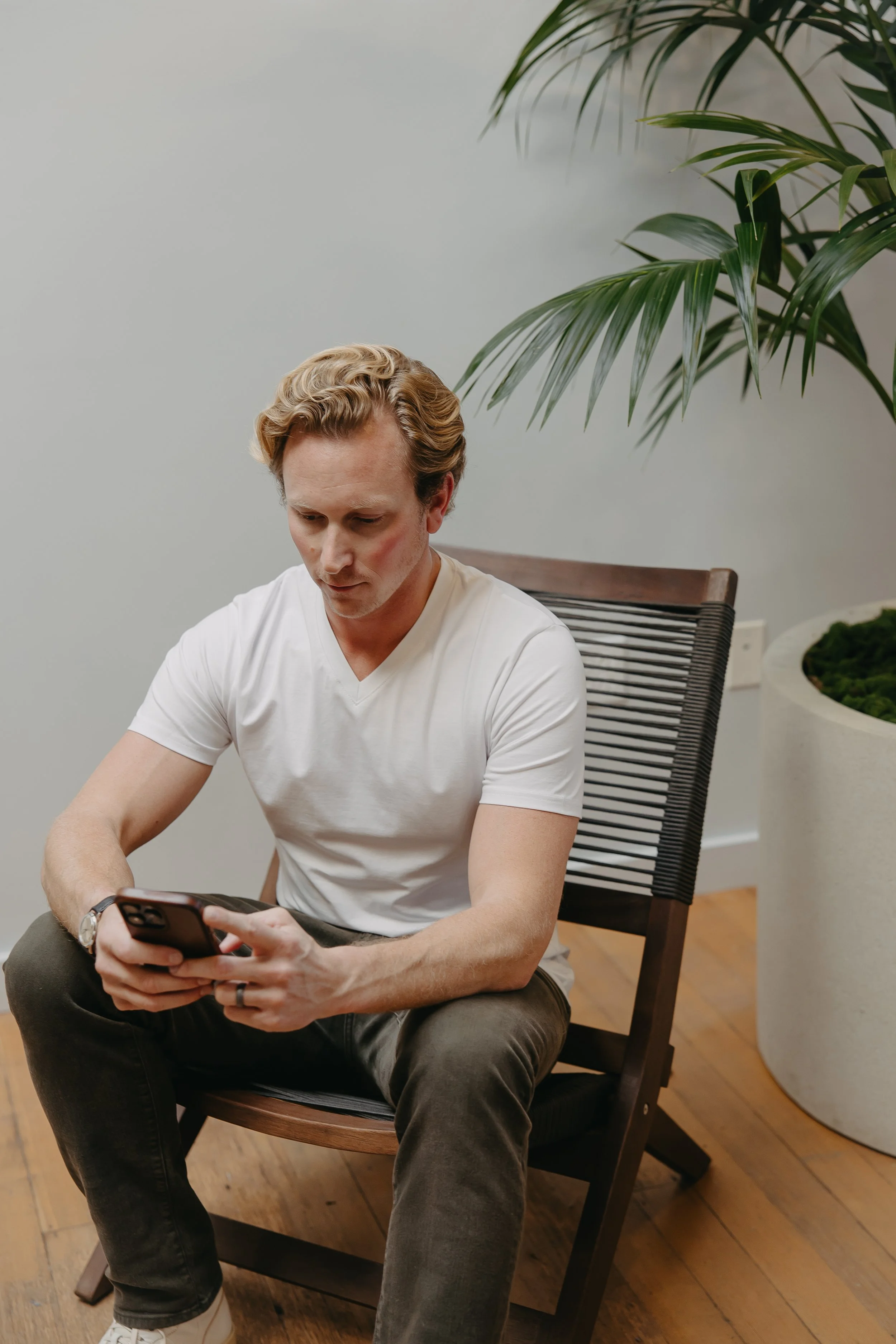 A man sitting in a modern room, looking at his phone with a serious expression.