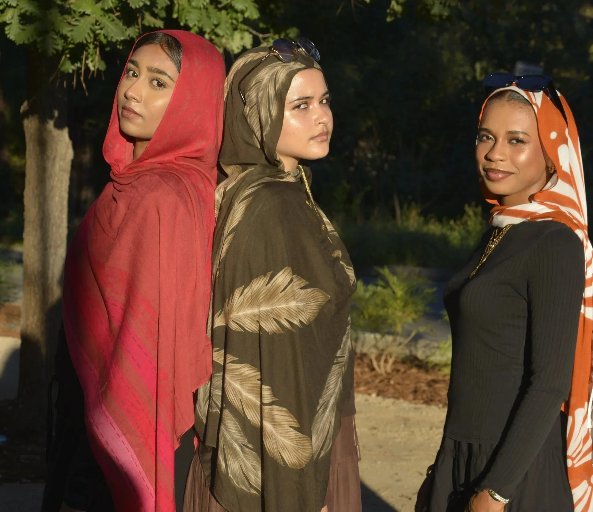 Three women wearing scarves and hoodies standing outside at night with trees in the background.