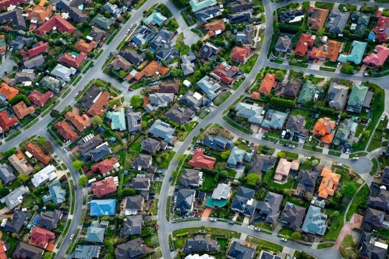 Aerial view of a suburban neighborhood with houses, lawns, streets, and trees.