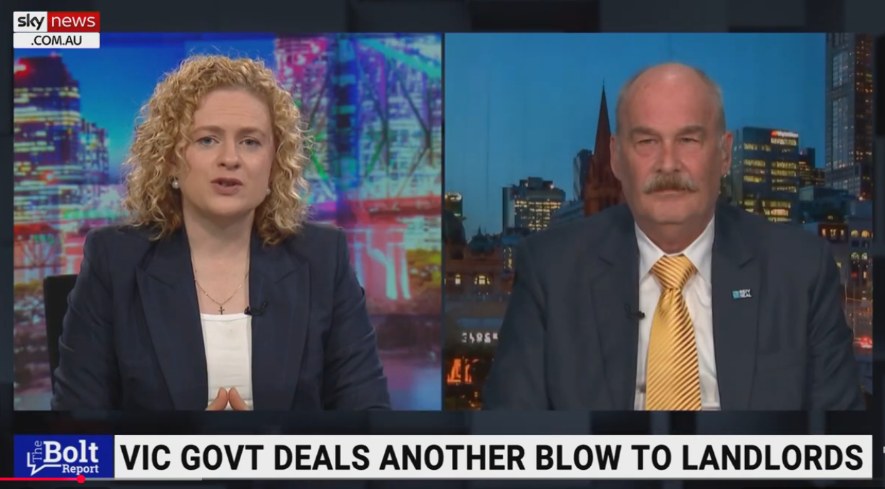 A split-screen television interview with a female news anchor on the left and a male interviewee on the right. Both are in news studio settings with cityscape backgrounds. The news ticker at the bottom reports on government dealings with landlords.