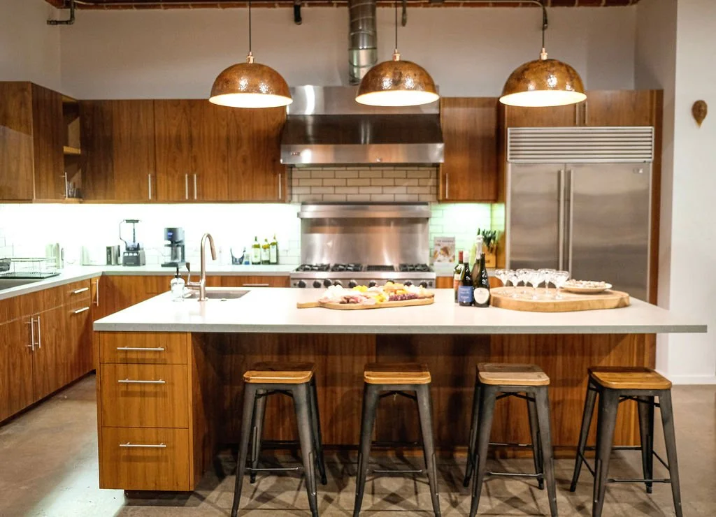 Modern kitchen with wooden cabinets, stainless steel appliances, a white island with stools, and copper pendant lights.