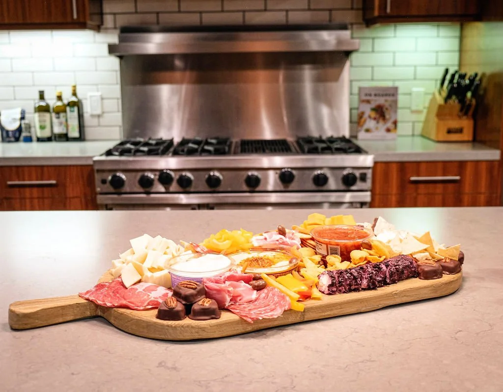 Charcuterie board with cheeses, meats, chocolates, and condiments on a kitchen counter with a stove in the background.