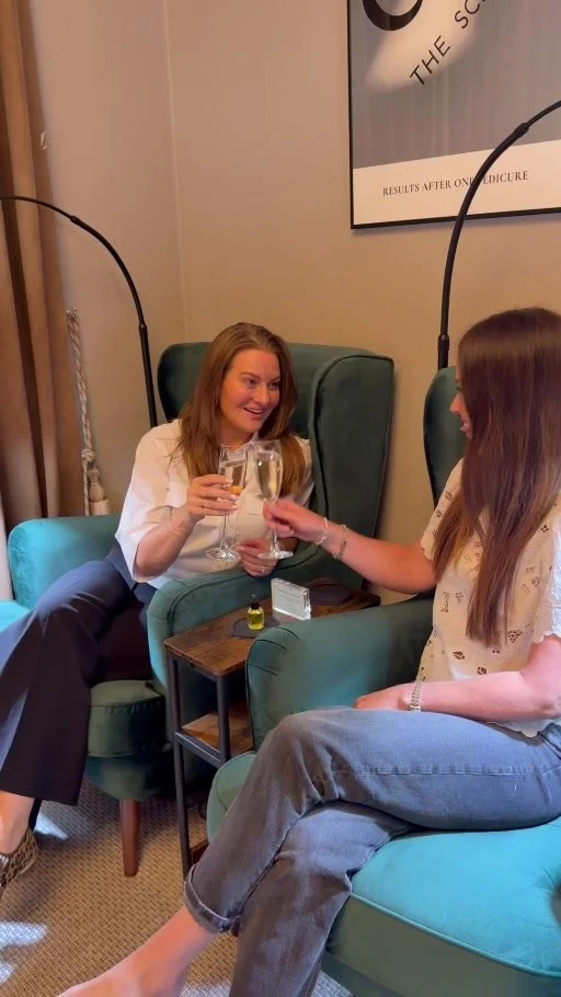 Two guests raising champagne glasses in the green pedicure chairs at Take Time, Cannizaro House.