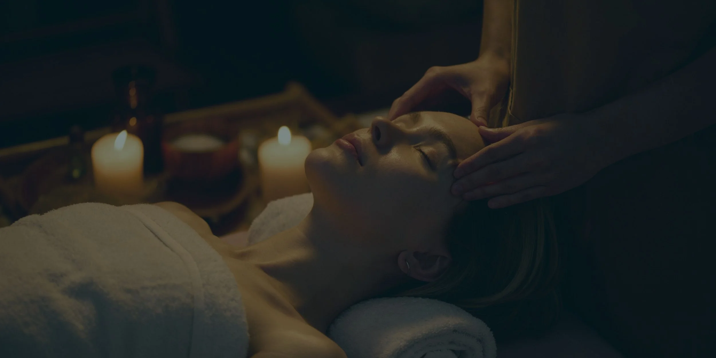 A woman receiving a facial massage in a spa setting with lit candles in the background.