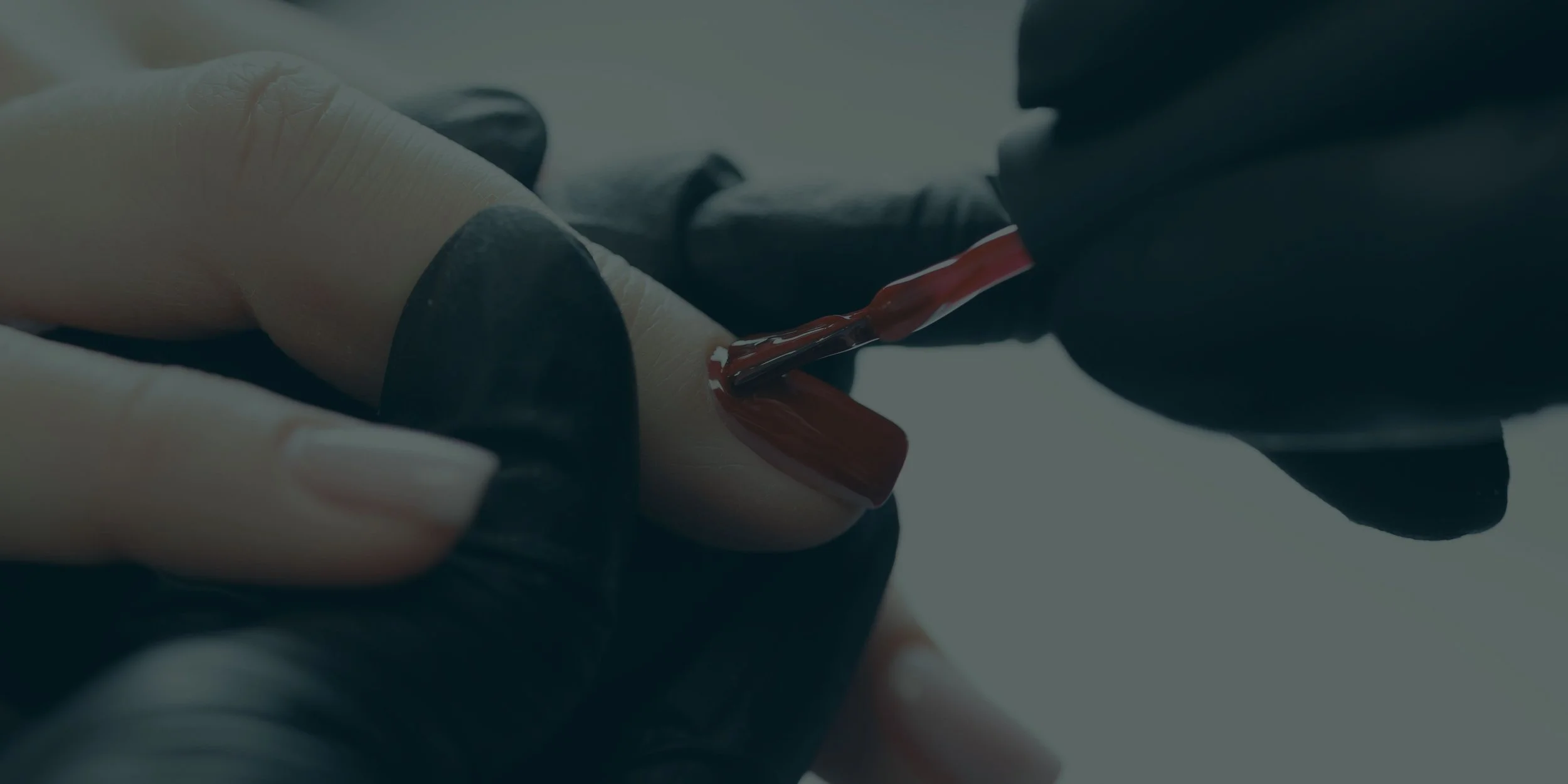 Close-up of a person applying red nail polish on their fingernail, wearing black gloves.