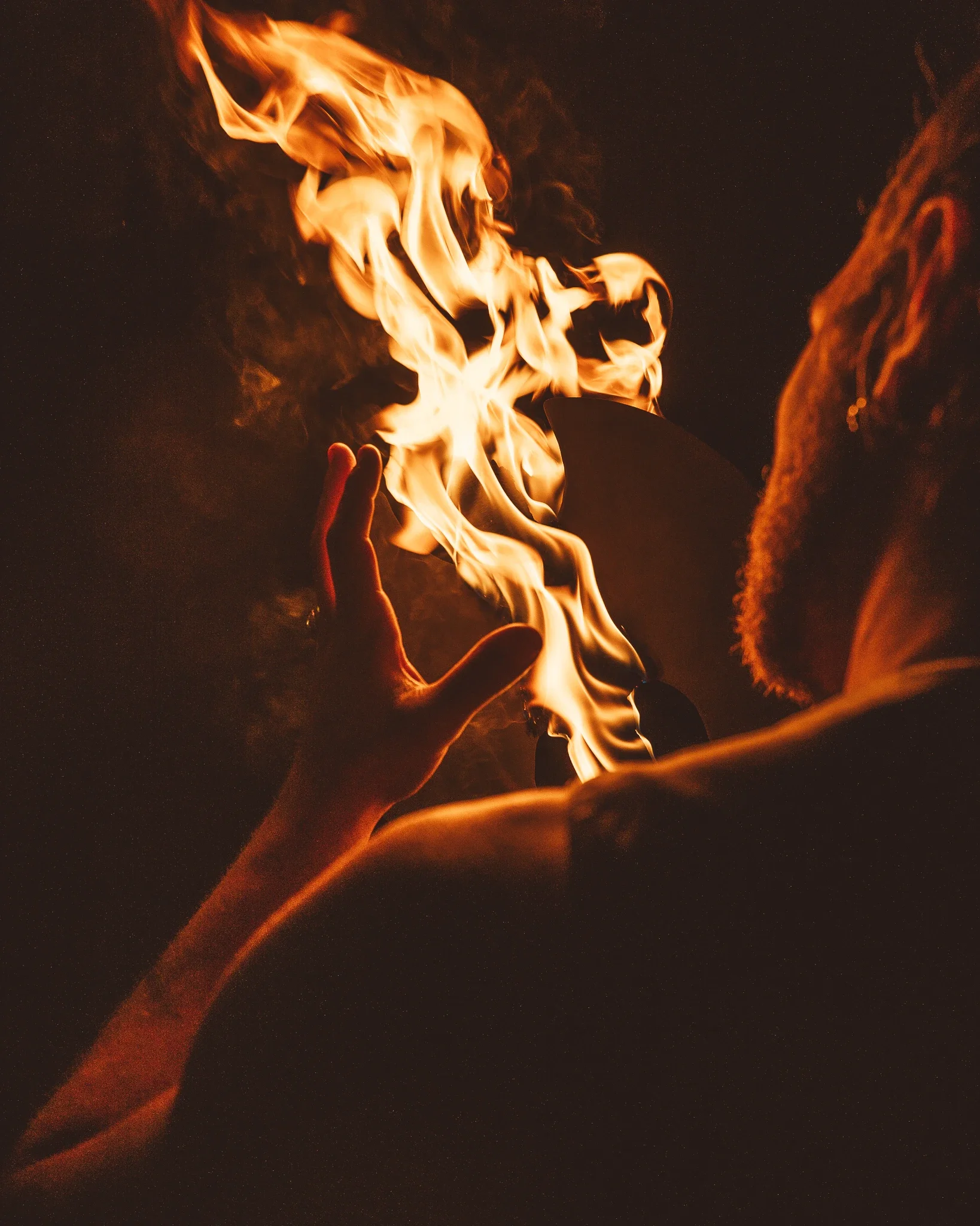 A person's hand holding a lighter flame in front of a dark background.