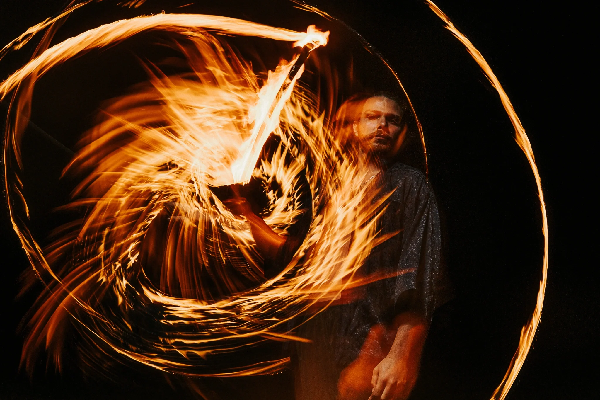 Person performing a fire dance, creating circular patterns of flames at night.