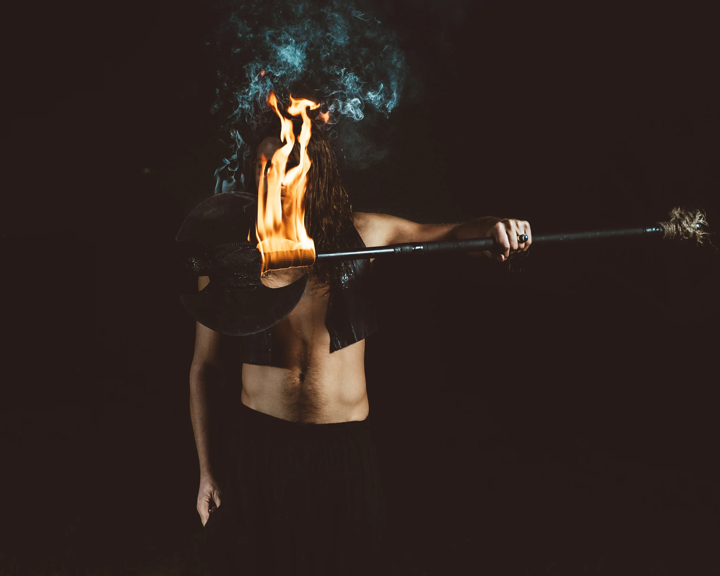 A person holding a torch with flames, with a dark background and smoke rising above their head.