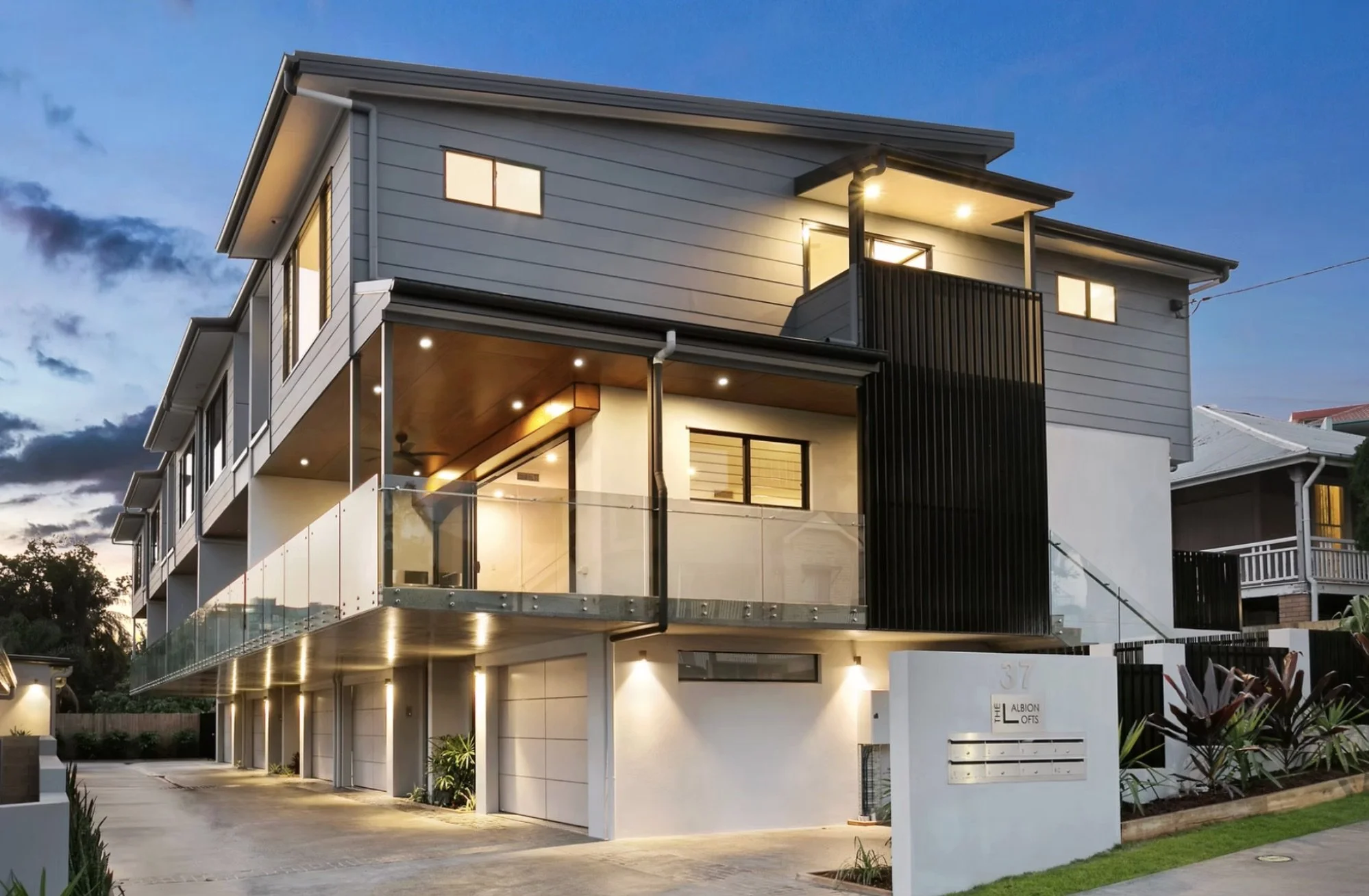 Modern multi-story apartment building at dusk with balconies and illuminated windows.