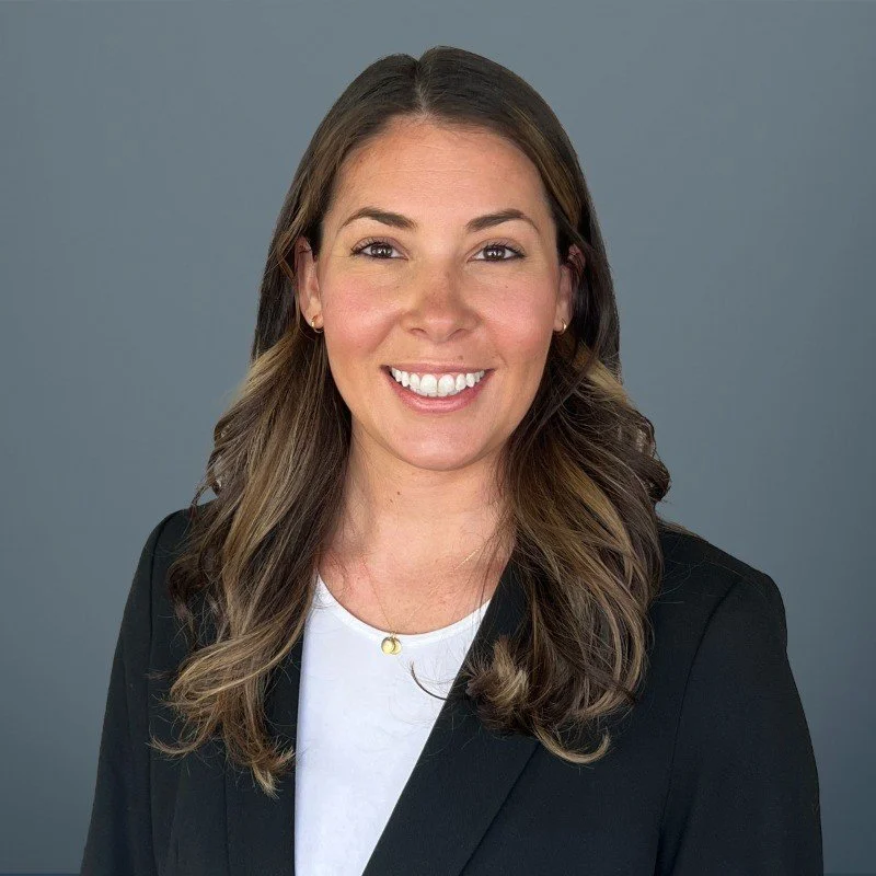 A middle-aged man with a beard and short hair is sitting on a bench in a neutral-colored room, wearing a brown polo shirt and cream-colored pants, looking thoughtful.