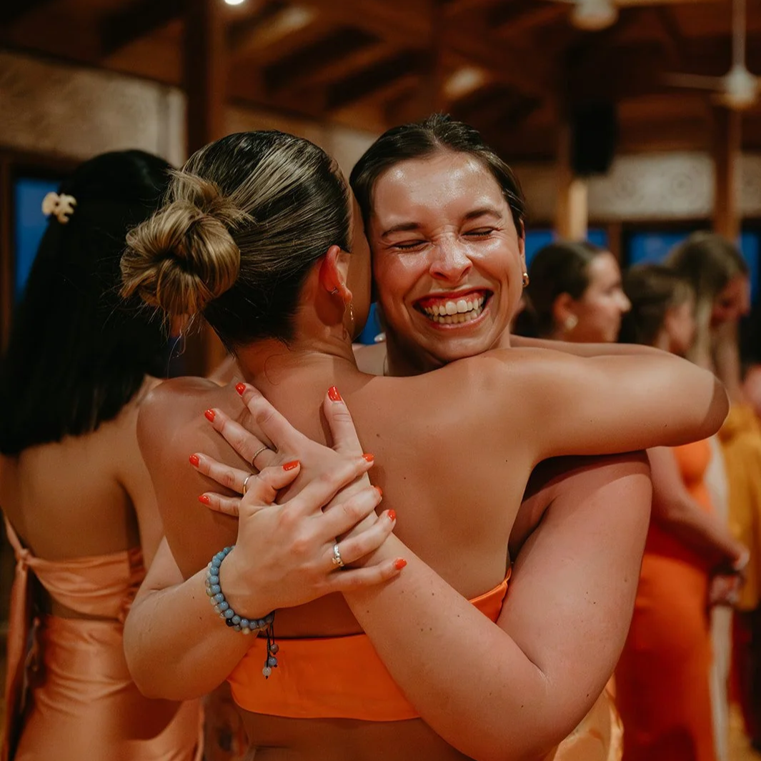 Two women embracing, smiling joyfully at a social event.
