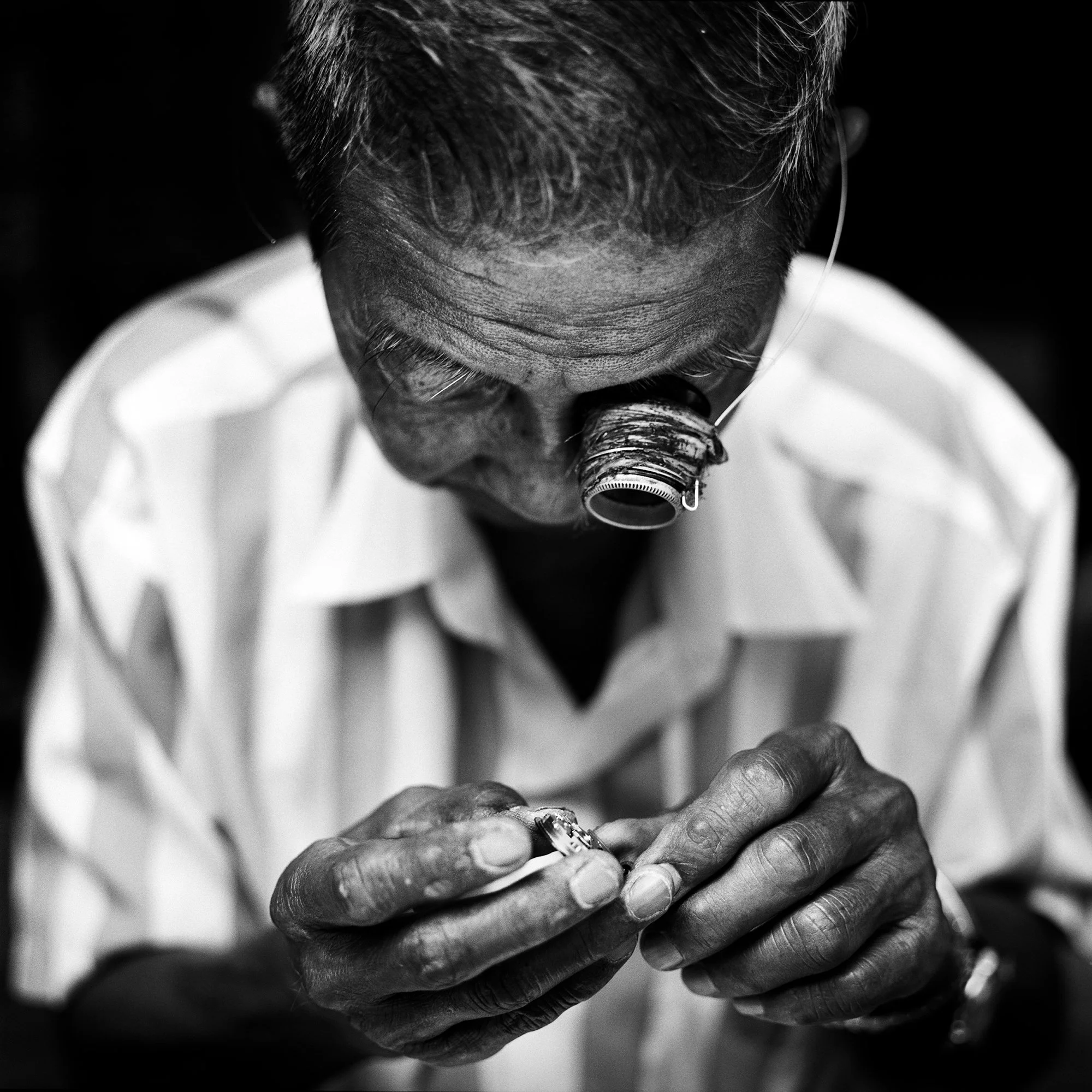 An example of an incredible Fine Art Photograph by renowned portrait photographer Colin I Homes. It shows man looking through a magnifying glass at a small object he is holding with his hands, focused on examining it closely.