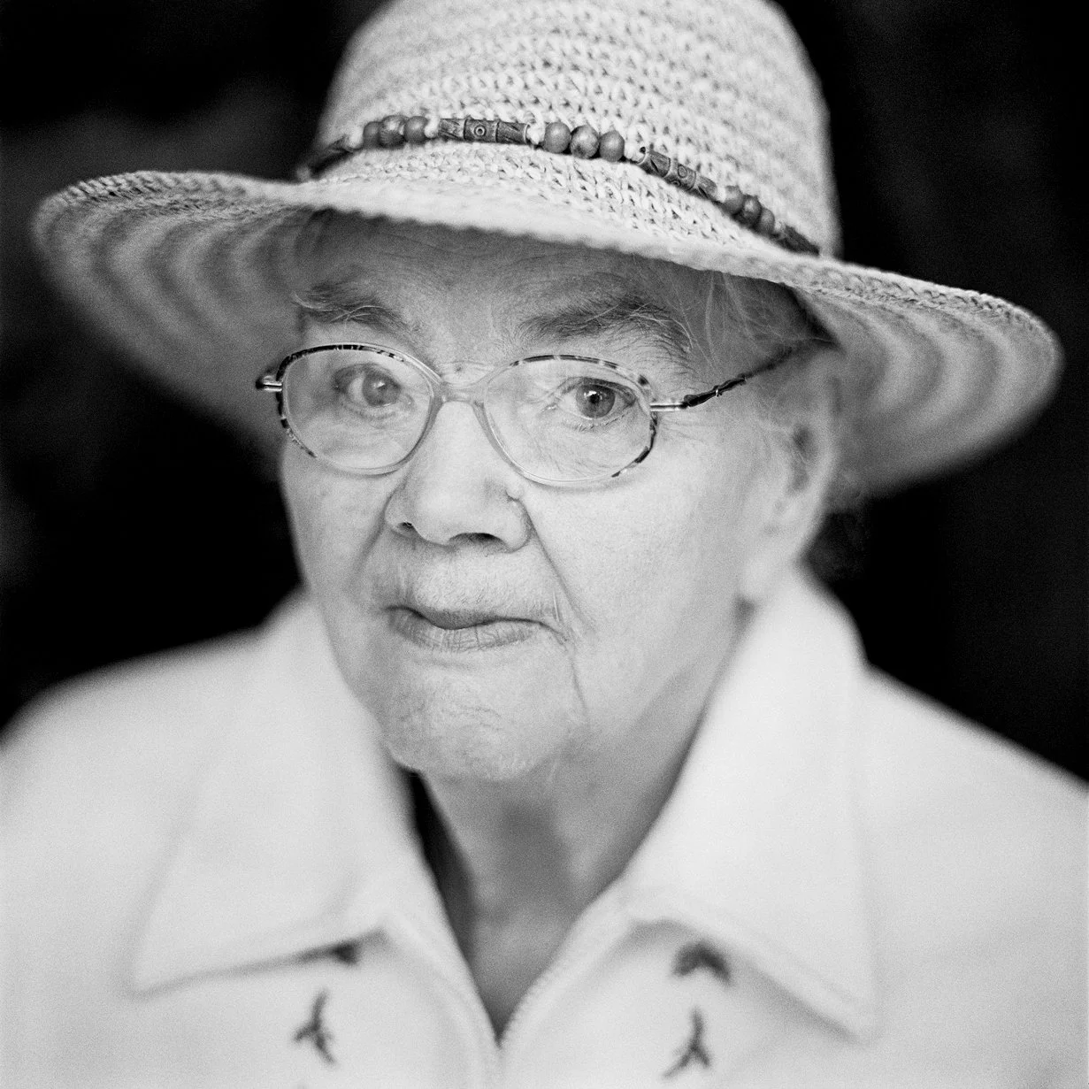 Black and white portrait of an elderly woman wearing glasses and a wide-brimmed hat with a beaded band. This was shot by Colin I Homes on a Hasselblad medium format film camera.