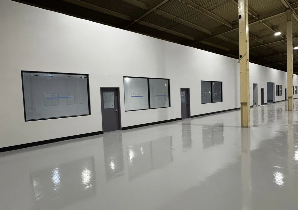 Empty industrial or warehouse interior with polished concrete floor, white walls, and large windows and doors.