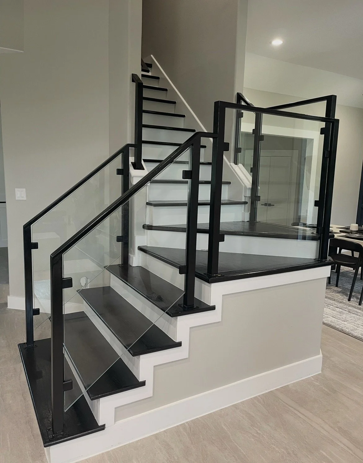 A modern staircase with black metal framing, glass panels for the railing, and dark wood steps, leading to an upper level in a contemporary home interior.