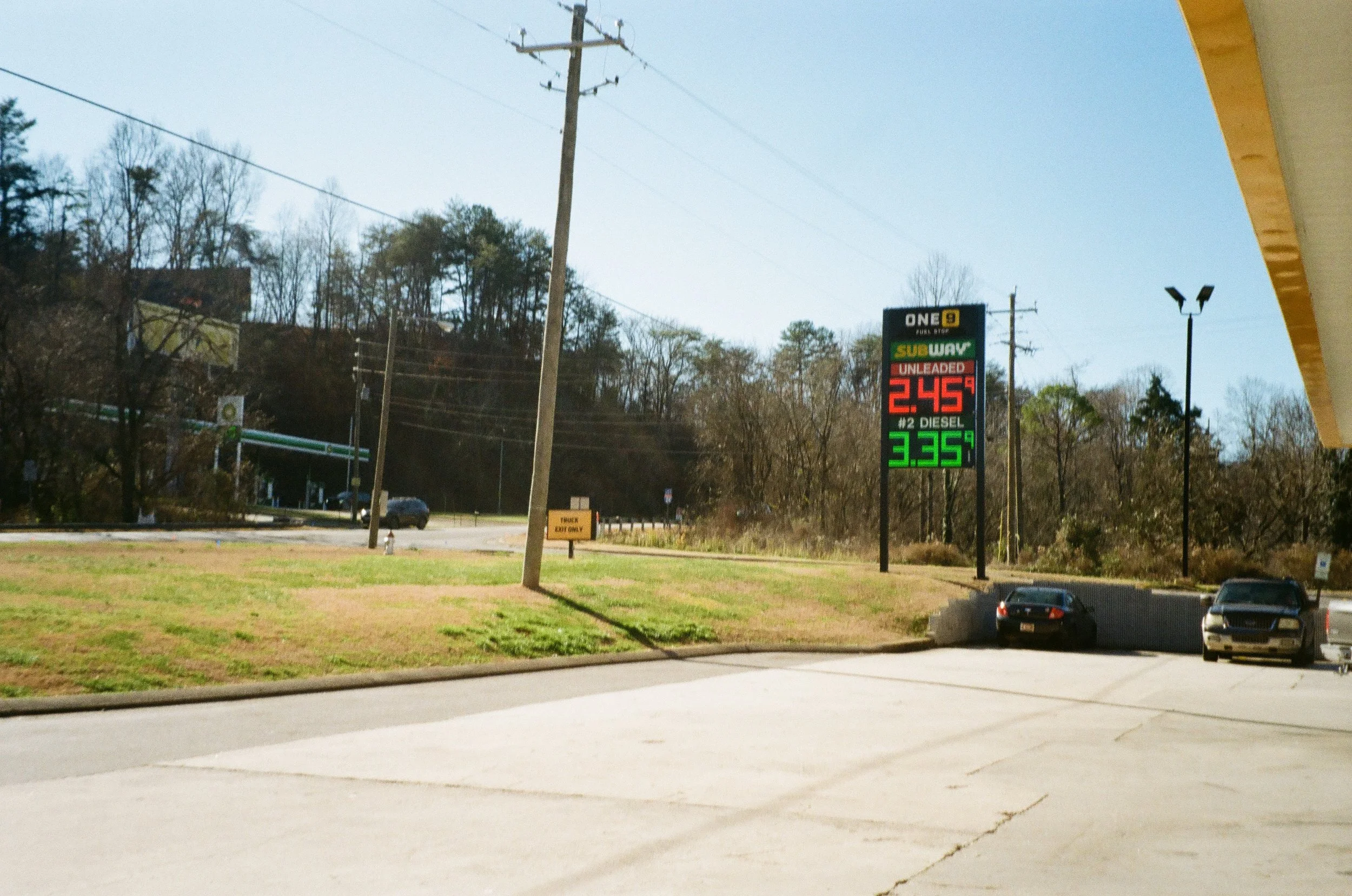 Film photo of a gas station sign displaying fuel prices: unleaded gas at $2.45 per gallon, diesel at $3.35 per gallon, with a Subway sign above.