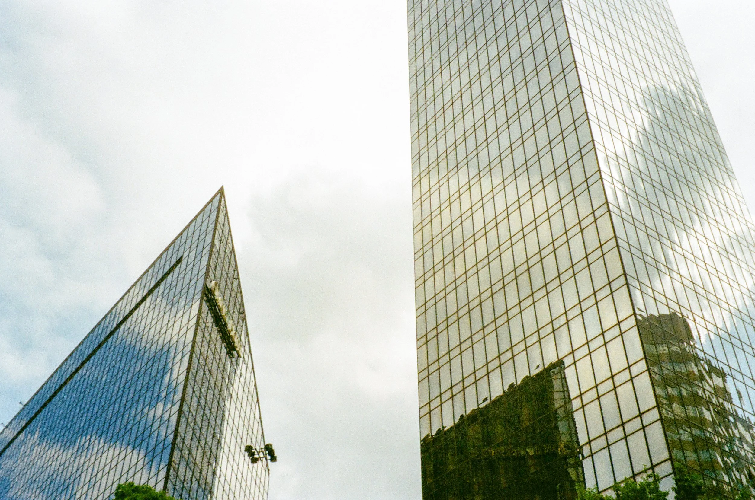 A film photo of two modern glass skyscrapers with reflective windows, one on the left and one on the right, against a cloudy sky.