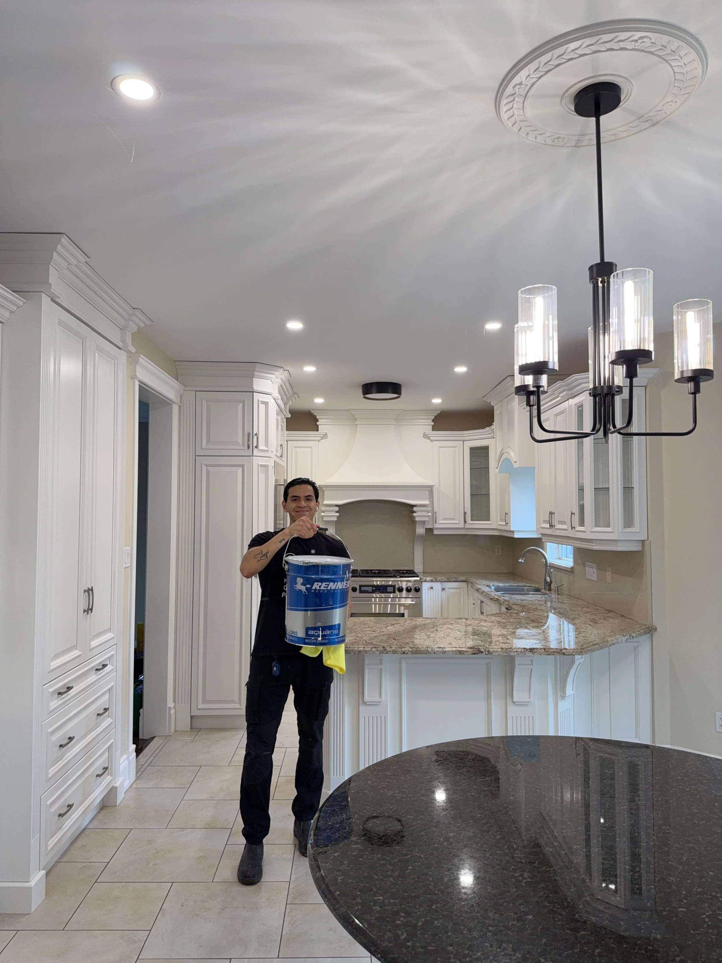 Man holding a bucket in a bright, white kitchen with granite countertops, white cabinetry, and a black chandelier.