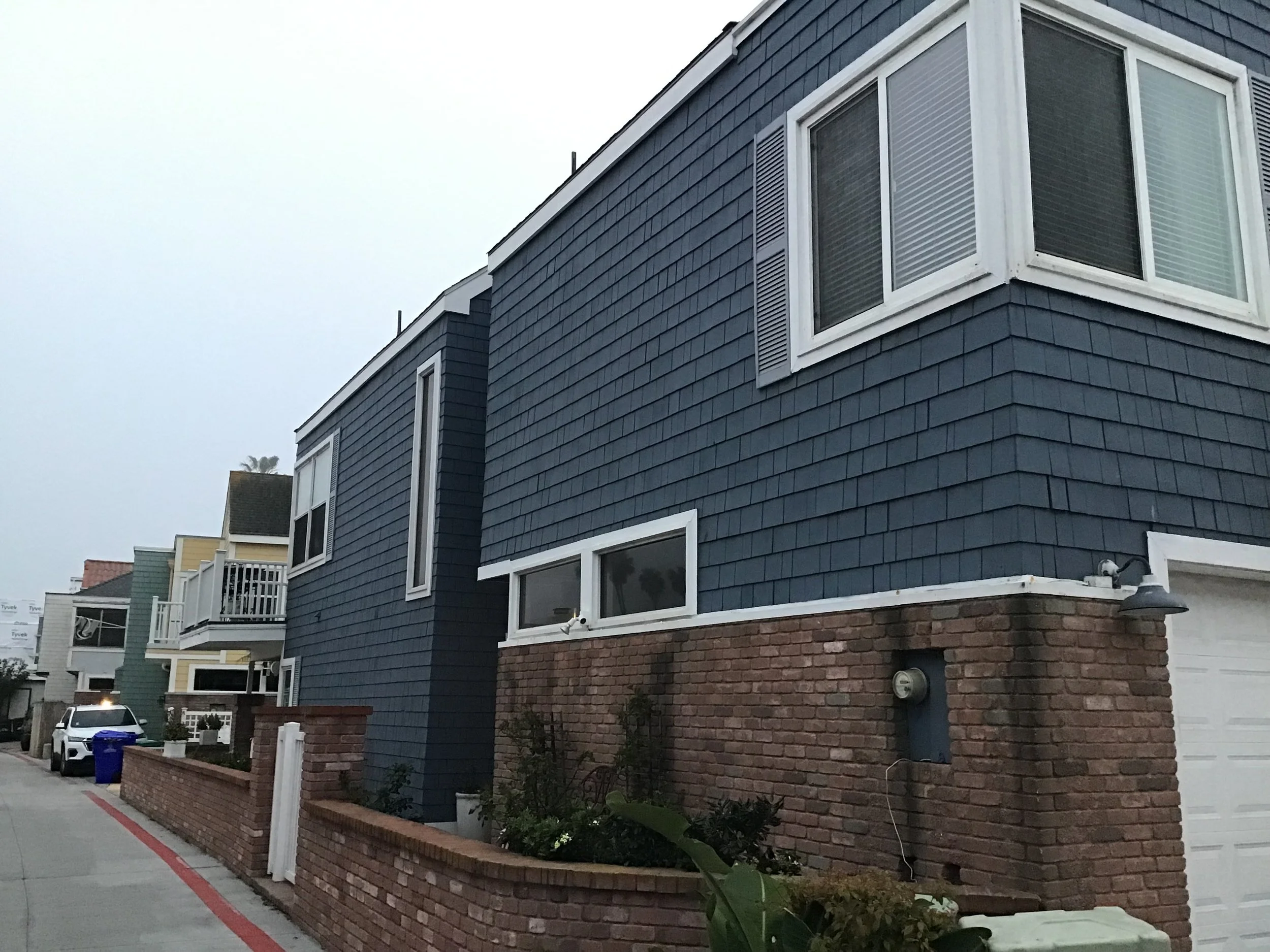 Side of a blue house with brick bottom, white trim, and bay windows on a cloudy day.