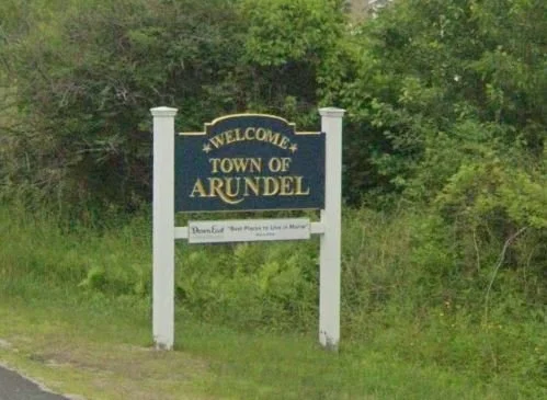 Welcome sign for the town of Arundel with a background of trees and greenery.