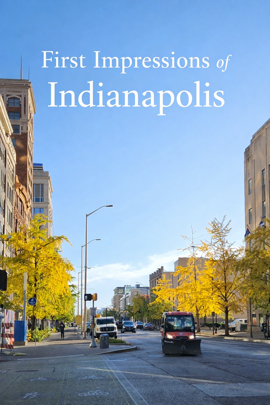 A downtown Indianapolis street in the fall, lined with golden trees, city buildings, and a clear blue sky.