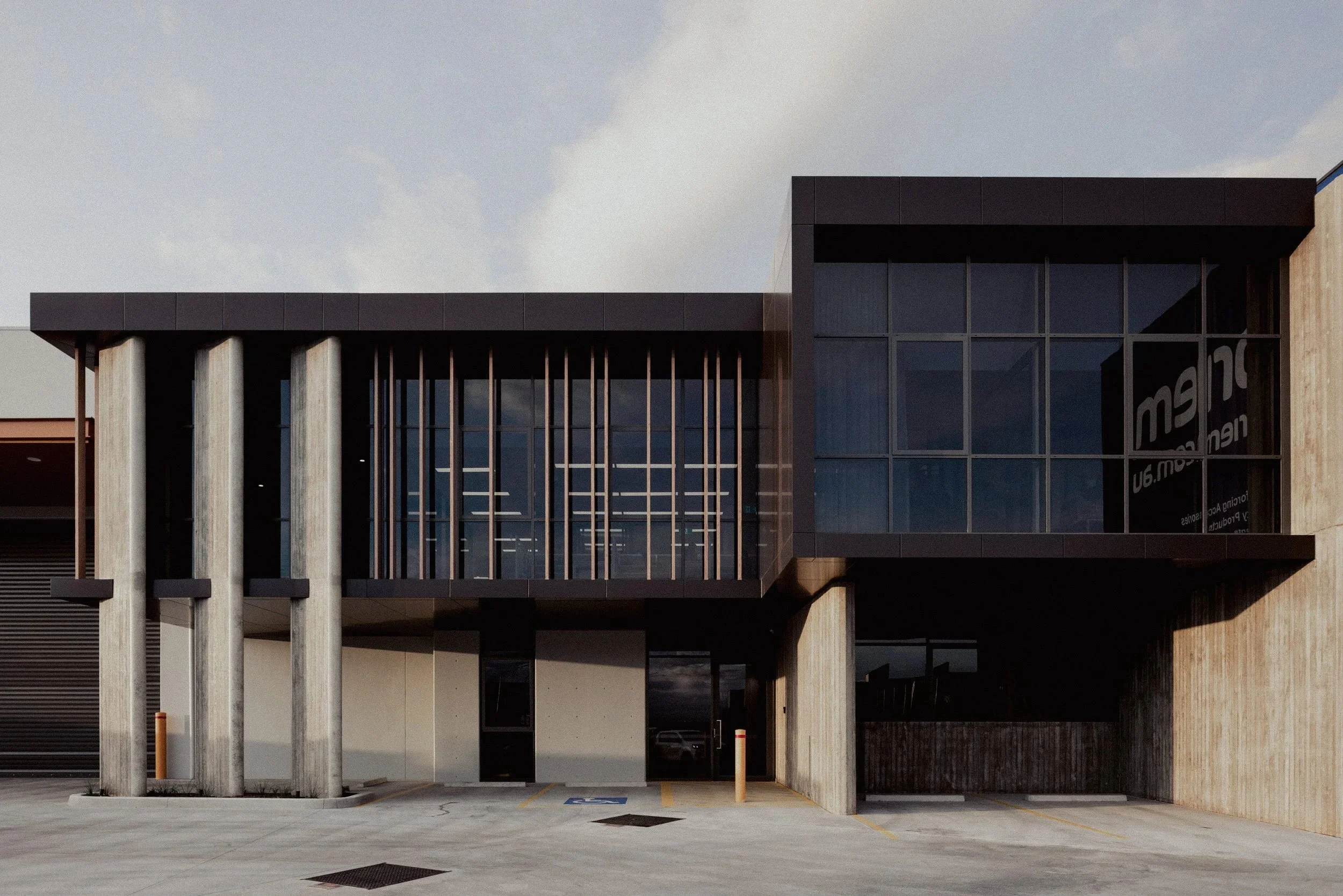 Modern commercial building with large glass windows and vertical concrete pillars, parking lot in front.