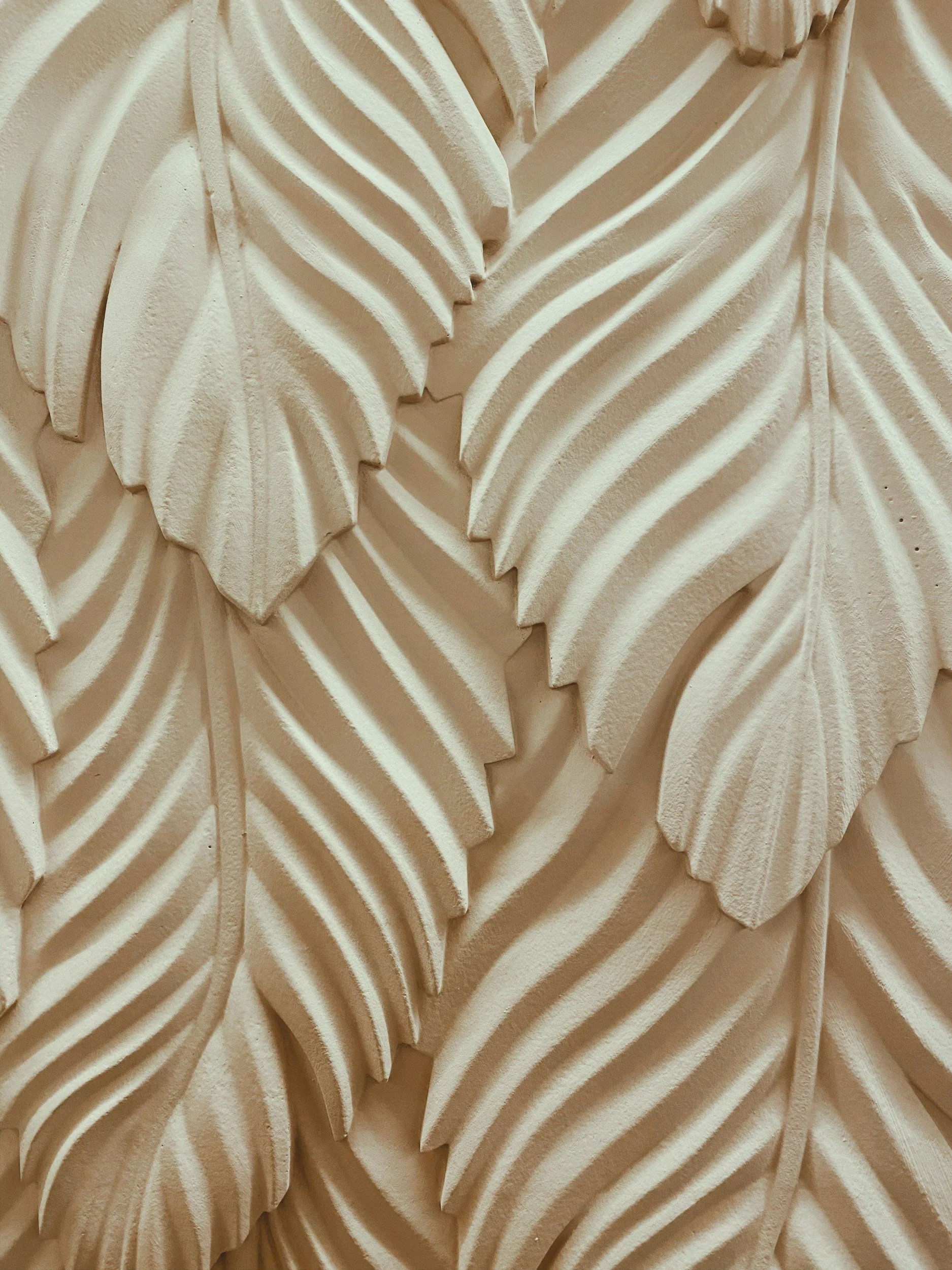 Close-up of a textured wall sculpture resembling overlapping leaves in beige and cream tones.