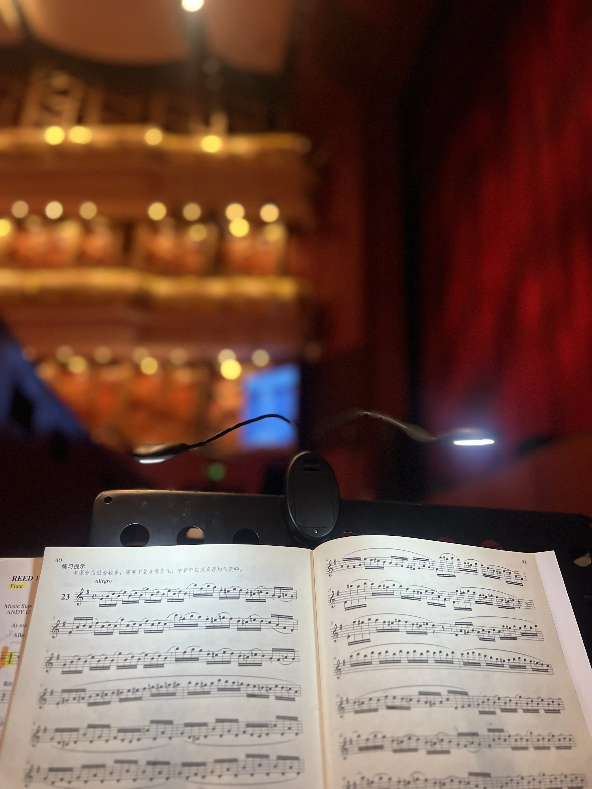 A music book open on a stand with sheet music, a microphone, and a red curtain in the background.