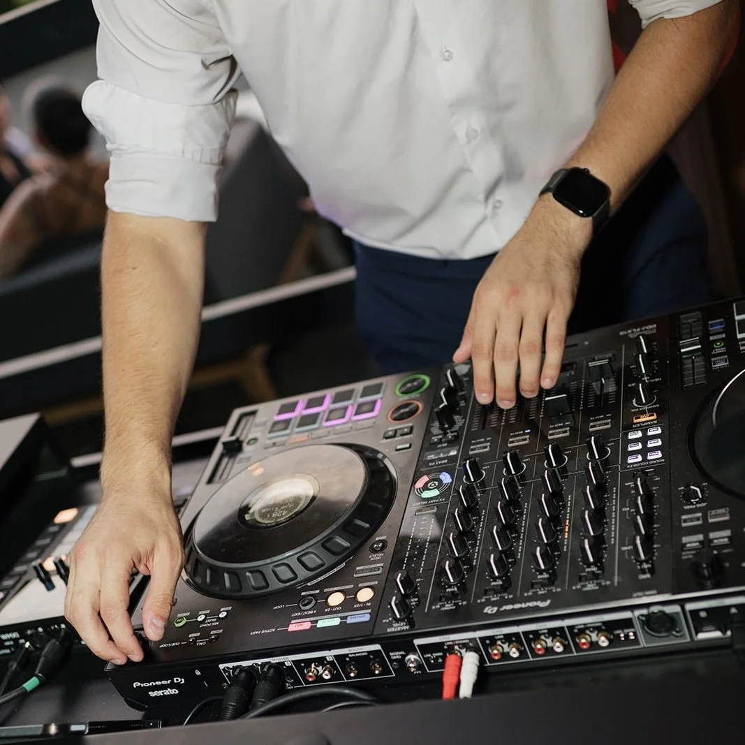 Person DJing with Pioneer DJ equipment, wearing a white shirt with rolled sleeves and a smartwatch, in a crowd setting.