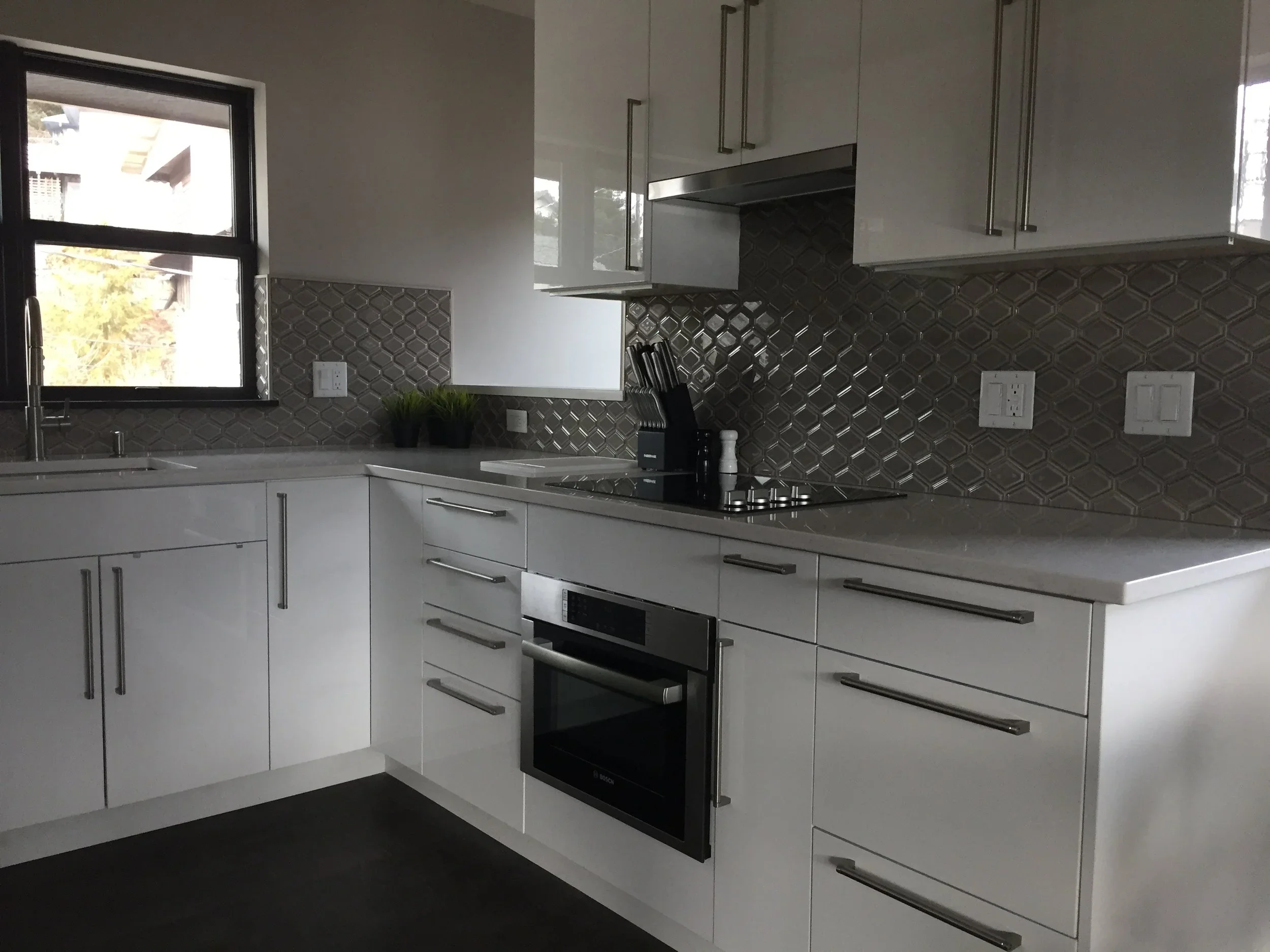 Modern kitchen with white cabinets, gray backsplash tiles, black appliances, and a double window above the sink.