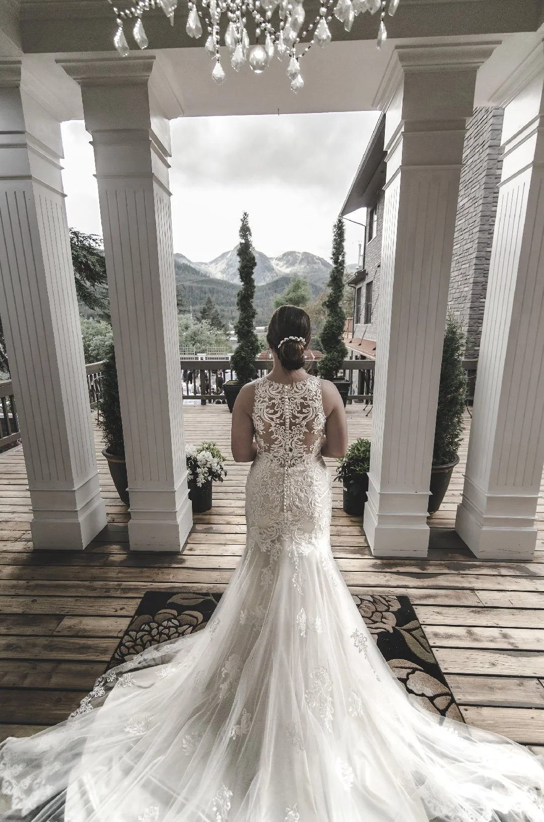 A bride in a lace wedding gown standing on a wooden porch with mountains in the background.