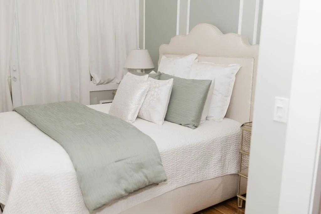 A neatly made bed with white and light gray pillows and a light gray blanket in a cozy bedroom.