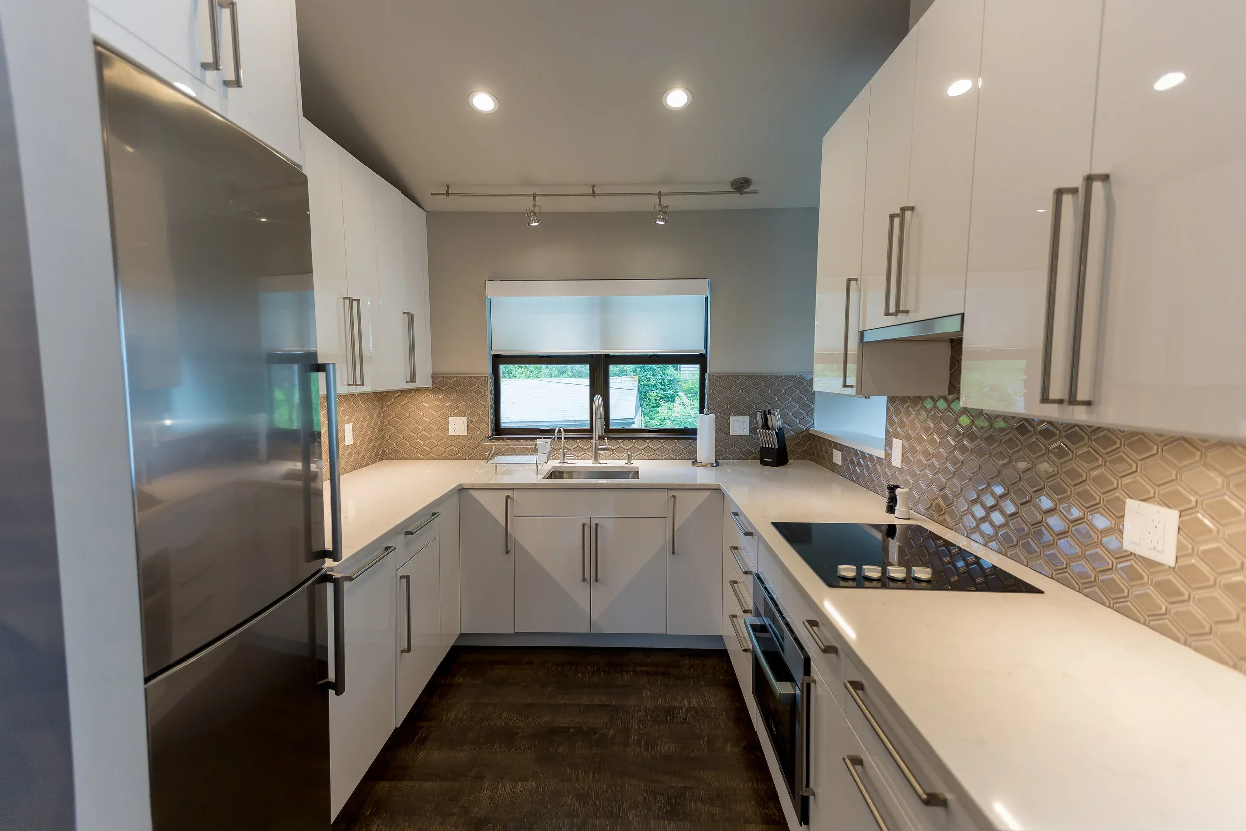 Modern kitchen with white cabinets, a black and white patterned backsplash, and a window above the sink.