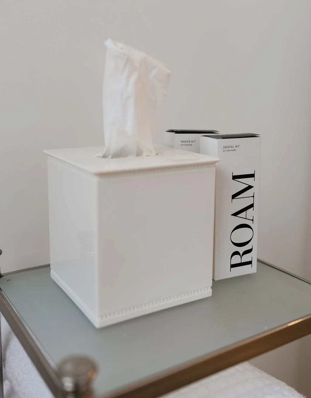 A tissue box with tissues and two boxed grooming kits, one labeled 'Shave Kit' and the other 'Dental Kit,' placed on a grey surface against a plain white background.