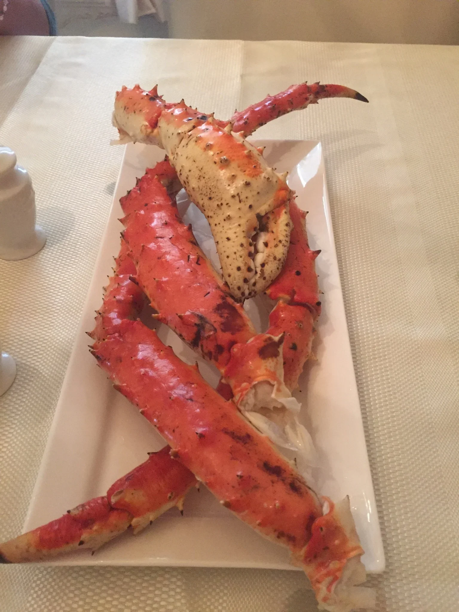 A plate with cooked lobster claws and body, sitting on a white rectangular dish on a table.