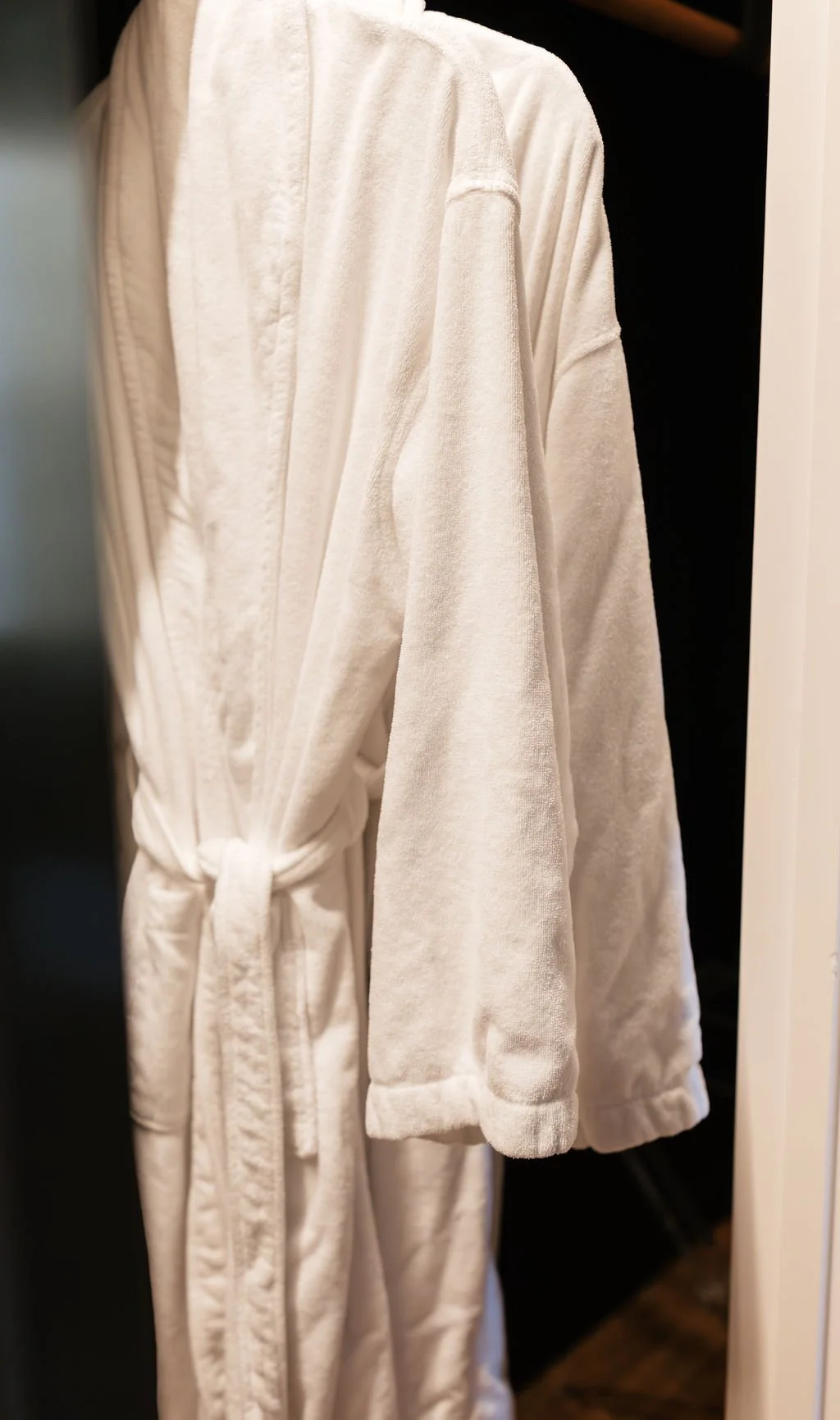 A white bathrobe hanging on a hook inside a closet or wardrobe.