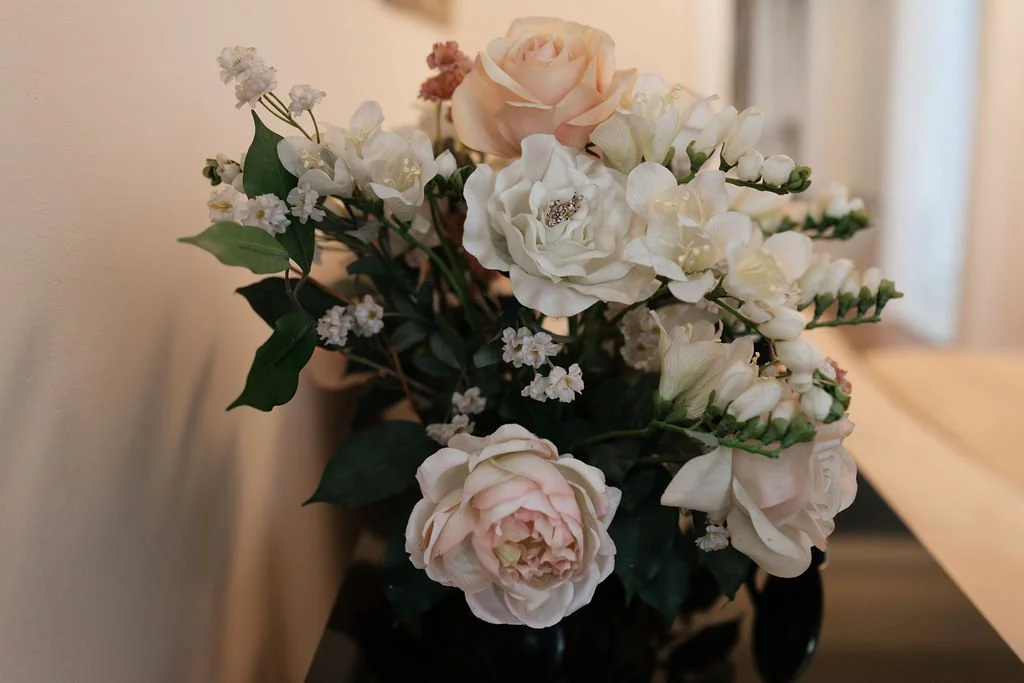 A floral arrangement with white, pink, and cream-colored flowers, including roses and other blossoms, in a black vase on a wooden table.