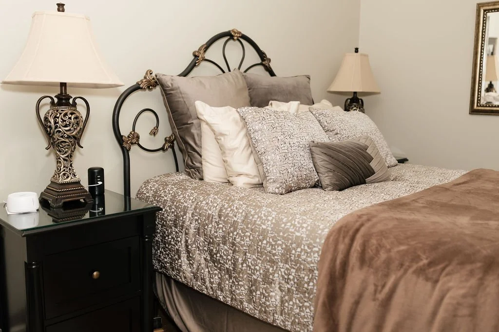 A neatly made bed with a decorative black metal headboard, multiple pillows, and a brown blanket. There are matching lamps on black nightstands on each side of the bed.