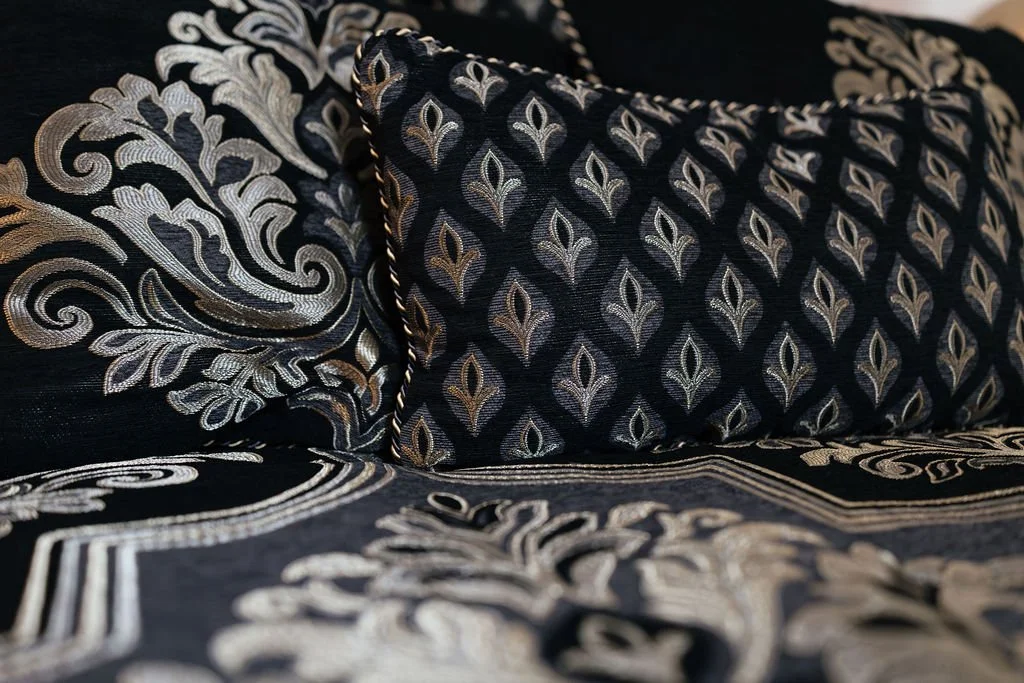 Close-up of decorative black and silver embroidered pillows and bedspread with intricate floral and geometric patterns.