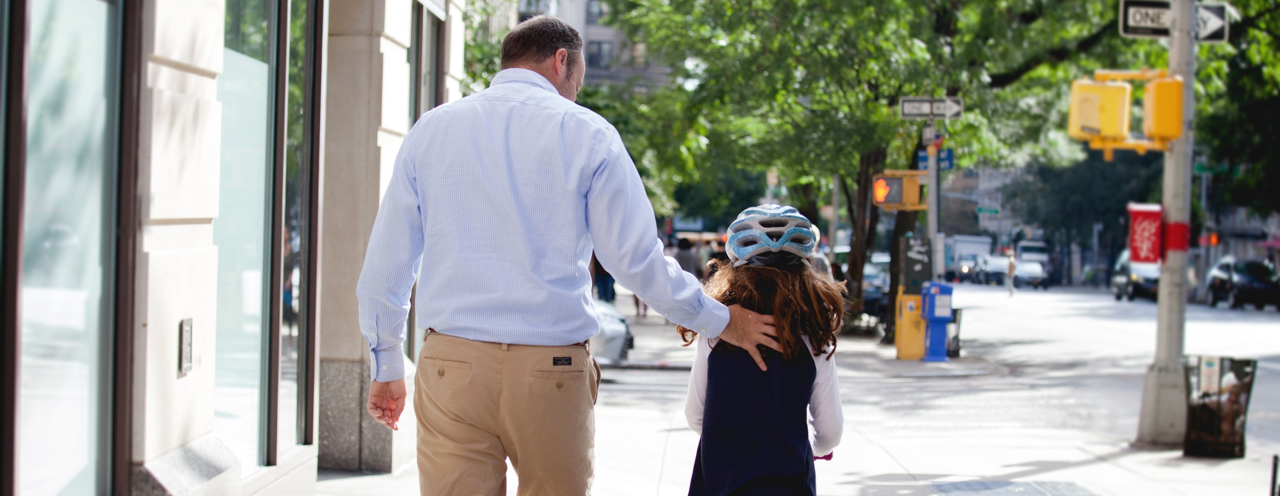 father walking daughter with helmet on down city street view from back