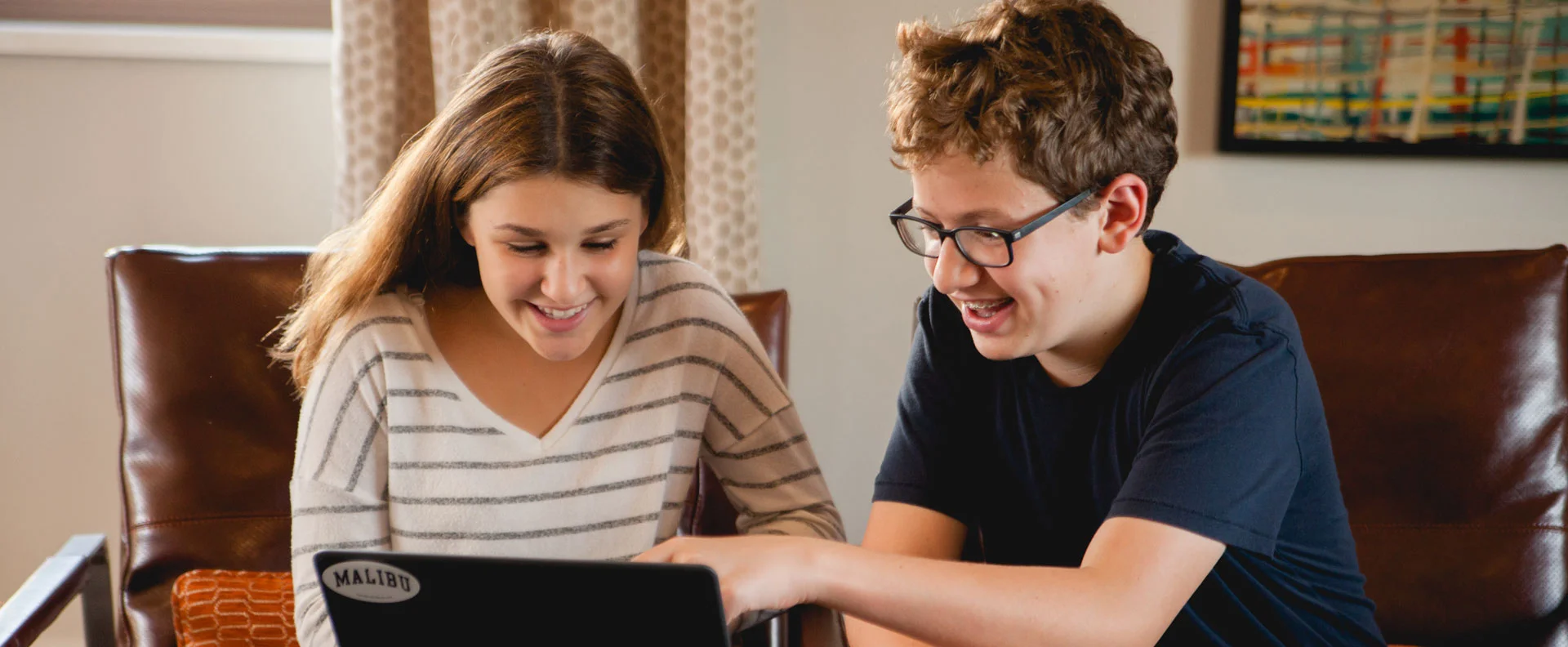two young teen kids smiling while looking at laptop computer